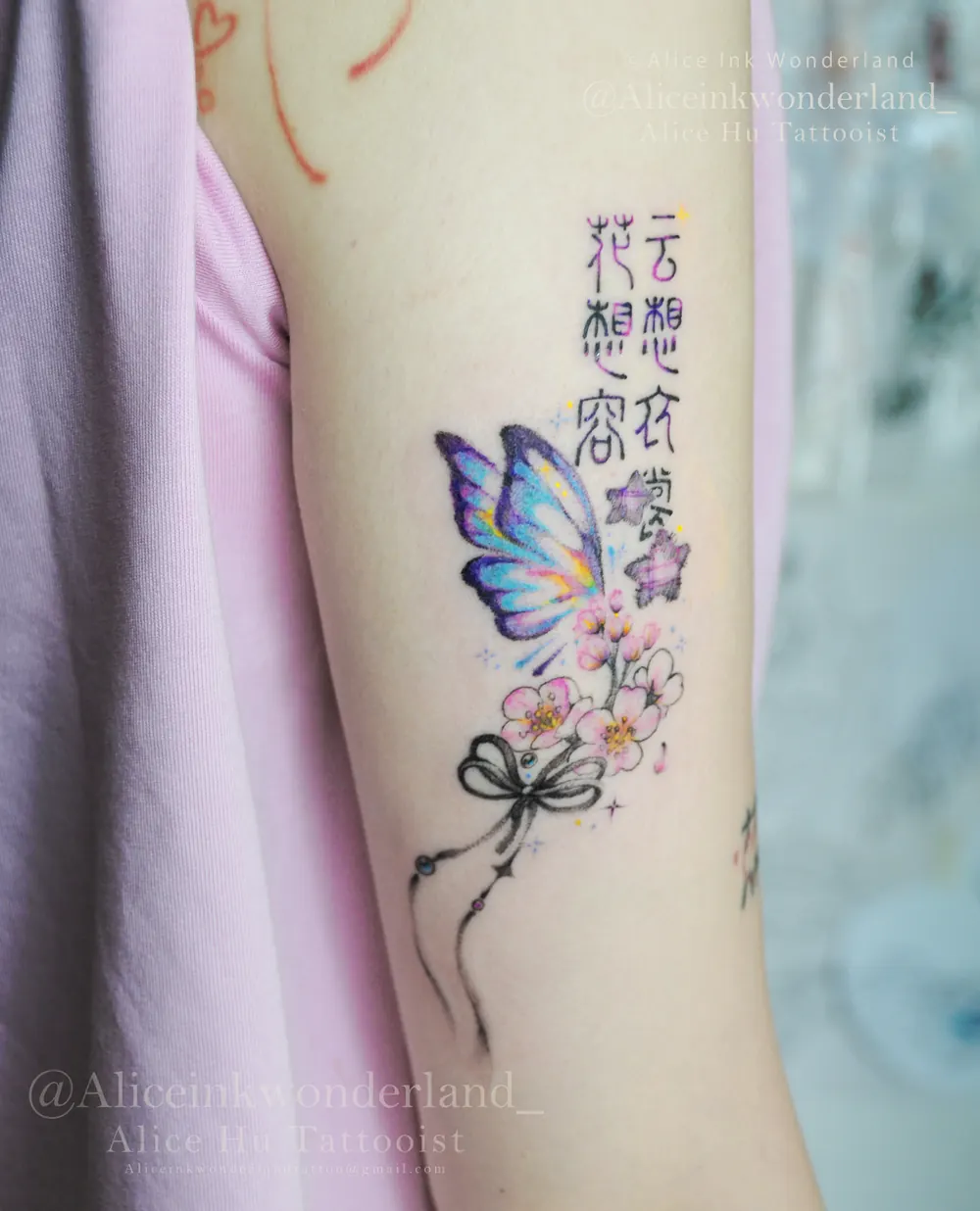 Custom colour tattoo of a butterfly, blossoms and script on an upper arm, by Alice Ink Wonderland